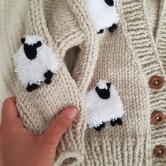 a hand holding two knit sheep mittens with buttons on the front and back of them