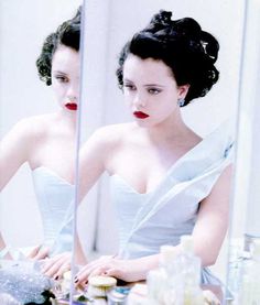 a woman sitting at a table in front of a mirror wearing a white dress and red lipstick