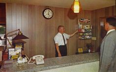 a man standing in front of a counter with a clock on the wall behind him