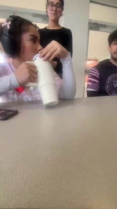 two people are sitting at a table and one is holding a roll of toilet paper