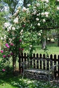 a wooden bench sitting under a tree next to a lush green park filled with pink and white flowers