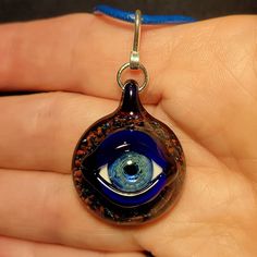 "Eyes have always been a fascination of mine. I make each handmade eye pendant using a blowtorch and Borosilicate glass in my studio. Some people refer to these eye pendants as Evil Eye Pendants. The evil eye has always been an ancient symbol that brings protection and good luck from any negative energy. I just like making eyes that look realistic, and glow from the silver in the glass. A lot goes into making these Evil Eye Pendants. First, I must create a murrini cane with the pupil and iris. I Handmade Spiritual Murano Glass Jewelry, Handmade Round Necklace With Eco-friendly Glass, Handmade Round Recycled Glass Necklace, Handmade Recycled Glass Necklaces, Unique Handmade Recycled Glass Necklaces, Handmade Glass Pendant Jewelry, Unique Murano Glass Necklaces As Gifts, Round Recycled Glass Necklaces For Gifts, Handmade Teardrop Glass Jewelry