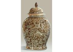 a brown and white vase with an ornate design on the lid, sitting against a gray background