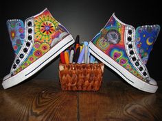 two pairs of colorful shoes sitting on top of a wooden table next to a basket with pencils and markers