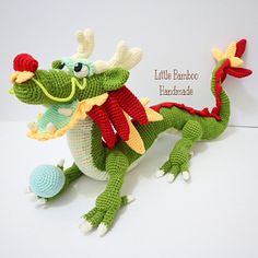 a crocheted green and red dragon stuffed animal sitting on top of a white surface