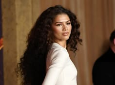 a woman with long, curly hair standing in front of a man wearing a suit