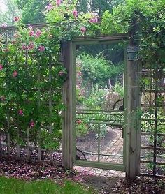 an open gate in the middle of a garden with pink flowers growing on it's sides