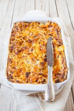 a white casserole dish with cheese and bread in it next to a knife