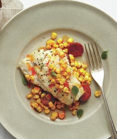 a white plate topped with food next to a fork and bowl filled with corn on top of it