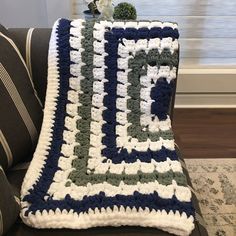 a crocheted afghan sits on a couch next to a vase with flowers in it