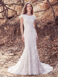 a woman in a white wedding dress standing on the ground with trees and bushes behind her