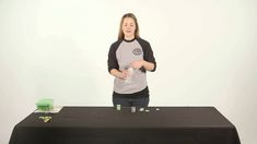 a woman standing behind a black table with green cups on it and a white wall in the background