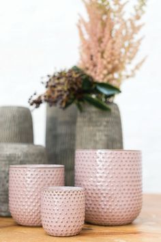 three gray vases sitting on top of a wooden table next to a pink flower