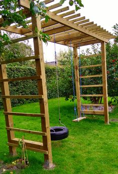 a wooden swing set with swings and a tire on the grass in front of it