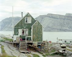 an old green house sitting on top of a hill next to the ocean with mountains in the background