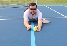 a man laying on the ground holding a tennis ball and racquet