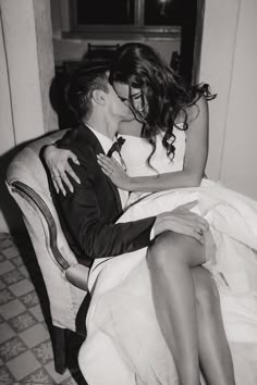 a man and woman sitting on top of a couch kissing each other in black and white