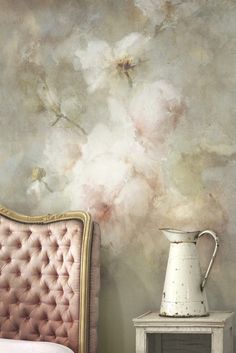 a white vase sitting on top of a table next to a pink chair and wall