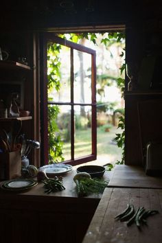 a table with plates and bowls on it in front of an open window that looks out onto the yard