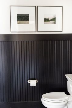 two framed pictures hang on the wall above a toilet in a black and white bathroom