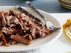 a white plate topped with meat covered in sauce and garnished with two serving utensils