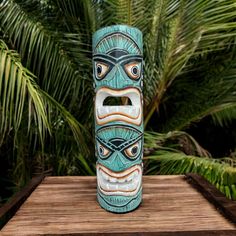 a tiki mask sitting on top of a wooden table in front of palm trees