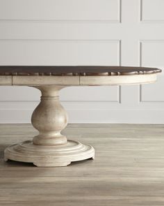 an oval dining table with wooden top and pedestals on the bottom, in front of a white painted wall