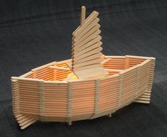 a boat made out of wooden sticks on top of a black surface with an umbrella sticking out of it