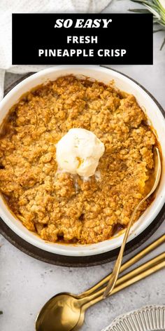 a white bowl filled with pineapple crisp on top of a table next to gold spoons