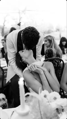 a man kissing a woman on the cheek in front of a table full of people