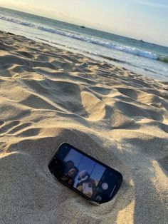 a cell phone laying in the sand at the beach with two people on it's screen