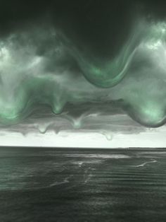 an image of some kind of green and black clouds in the sky over the ocean