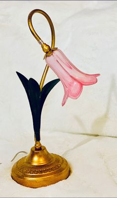 a pink flower is sitting on top of a brass stand with a hook in the middle