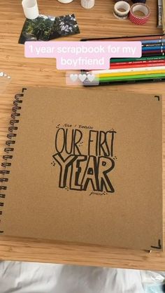 an open notebook sitting on top of a wooden table next to markers and pencils