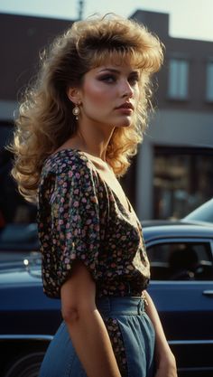 Woman wearing a blouse with bold prints and high-waisted jeans, with voluminous 80s hairstyle, standing by a classic car 80s Womens Hair, 80s Hairstyles For Long Hair, Classic 80s Fashion, Late 80s Fashion, 80s Fashion Dresses, 80 S Hairstyles, Voluminous Hairstyles, Vintage Hairstyle