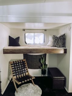 a room with a chair, window and shelf above it that is filled with pillows