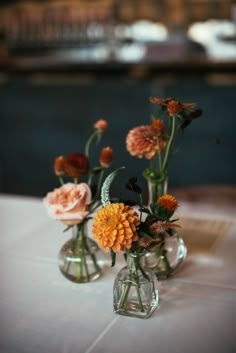 three vases filled with flowers sitting on top of a white tablecloth covered table