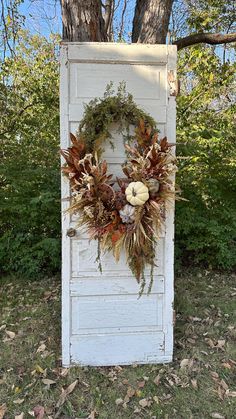 an old door decorated with wreaths and fake leaves in front of a large tree