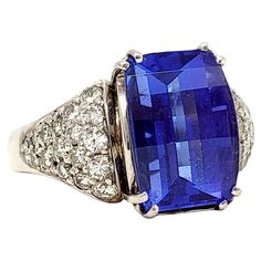 Ring size: 10 Absolutely magnificent tanzanite and diamond ring. The brilliant blue stone against the bright white diamonds really catches the viewers eye while the sizeable stone fills the finger with sparkle. The impressive 7.50 carat prong set rectangular dome step cut tanzanite stone sits at the very center of the piece, demanding the viewers attention. It is a gorgeous, transparent violetish-blue color. Flanking the main stone are 2 triangular shaped clusters of pave diamonds totaling 1.20 Emerald Cut Tanzanite Diamond Ring, Luxury Tanzanite Diamond Ring With Emerald Cut, Blue Tanzanite Diamond Ring With Diamond Accents, Blue Tanzanite Diamond Ring With Accents, Blue Rectangular Diamond Ring For Formal Occasions, Brilliant Cut Tanzanite Gemstones, Formal Blue Tanzanite Gemstones, Rectangular Blue Diamond Ring, Formal Tanzanite Diamond Ring With Diamond Accents