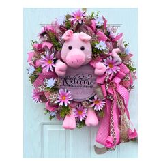 a pink wreath with a pig on it and flowers in the middle is hanging on a door