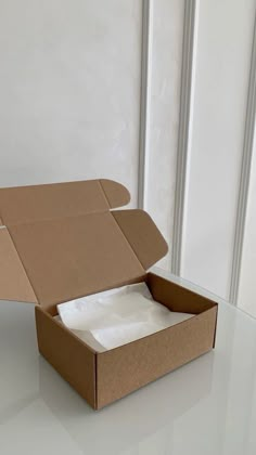 an open cardboard box with tissue paper in it on a white table next to a wall