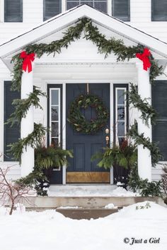 the front door is decorated with evergreen wreaths and red bows