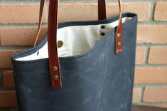 a blue bag sitting on top of a wooden table next to a brick wall with leather handles