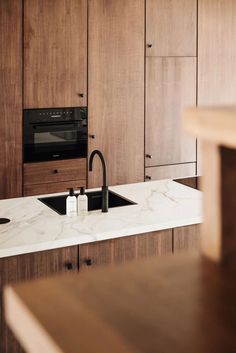 a kitchen with marble counter tops and wooden cabinets, black faucet on the sink