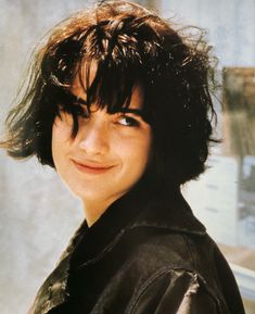 a close up of a person wearing a black jacket and smiling at the camera with long hair