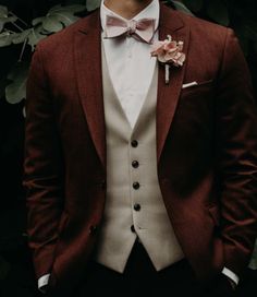 a man in a suit and bow tie standing next to some plants with his hands in his pockets