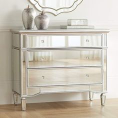 a mirrored dresser with two vases on top