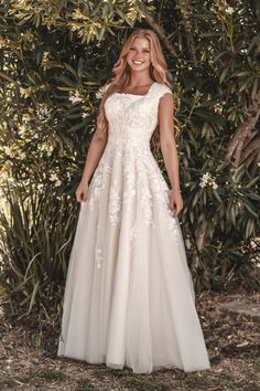 a woman standing in front of some trees wearing a wedding dress