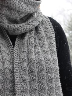 a woman wearing a gray scarf and black top in the snow with trees behind her