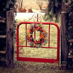 a red gate with a wreath on it in front of a grassy field and trees